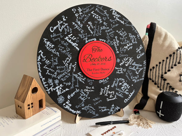 Vinyl music record lookalike sign used as a wedding guest book with personalized names, date and special song title and artist engraved in the middle. The wedding guests sign the record 