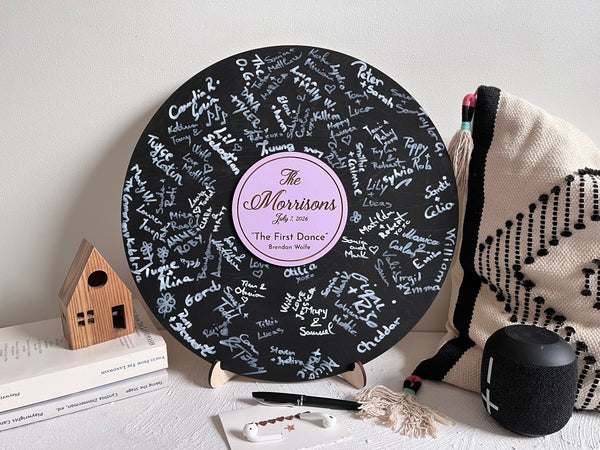 Vinyl music record lookalike sign used as a wedding guest book with personalized names, date and special song title and artist engraved in the middle. The wedding guests sign the record 