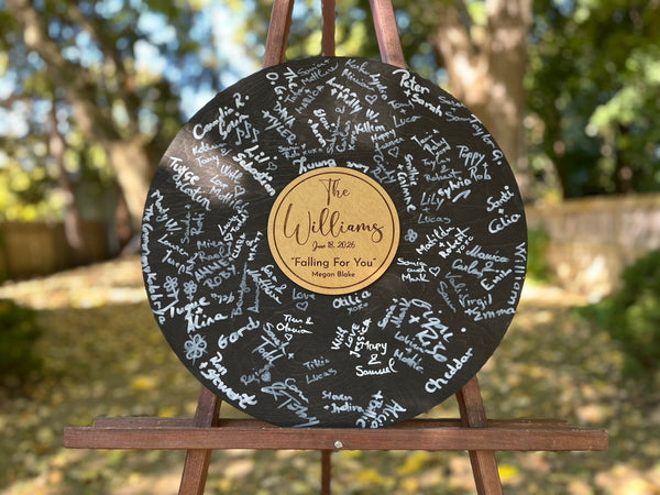 Vinyl music record lookalike sign used as a wedding guest book with personalized names, date and special song title and artist engraved in the middle. The wedding guests sign the record 