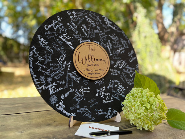 Round black wooden music record used as a wedding guest book for guest signatures. Personalized with the last name of the couple, a wedding date as well as a favourite song and artist, engraved in the middle of the record, to mimic a musical vinyl record.