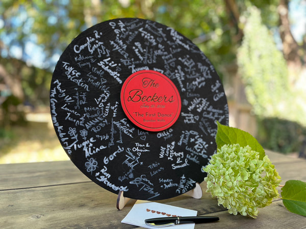 Vinyl music record lookalike sign used as a wedding guest book with personalized names, date and special song title and artist engraved in the middle. The wedding guests sign the record 
