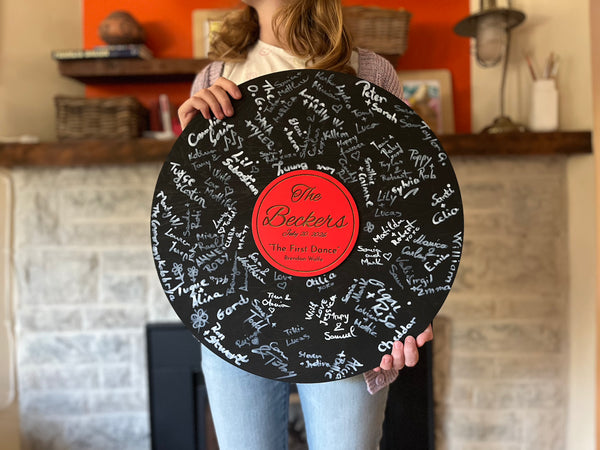 Vinyl music record lookalike sign used as a wedding guest book with personalized names, date and special song title and artist engraved in the middle. The wedding guests sign the record 