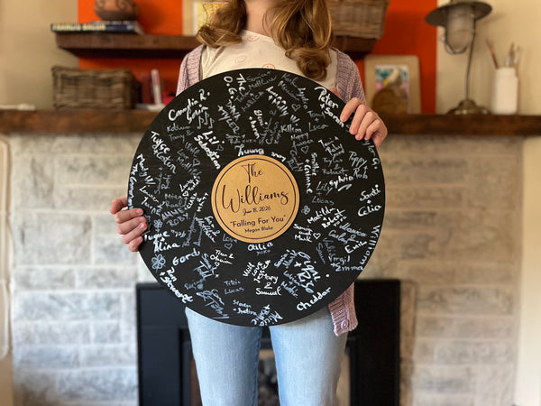 Vinyl music record lookalike sign used as a wedding guest book with personalized names, date and special song title and artist engraved in the middle. The wedding guests sign the record 