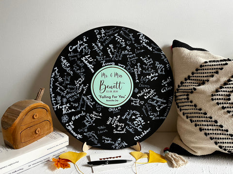 Vinyl music record lookalike sign used as a wedding guest book with personalized names, date and special song title and artist engraved in the middle. The wedding guests sign the record 