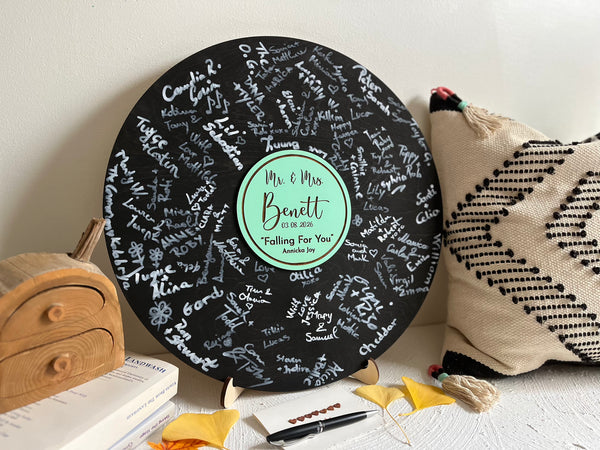 Vinyl music record lookalike sign used as a wedding guest book with personalized names, date and special song title and artist engraved in the middle. The wedding guests sign the record 