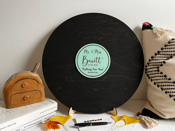 Vinyl music record lookalike sign used as a wedding guest book with personalized names, date and special song title and artist engraved in the middle. The wedding guests sign the record 