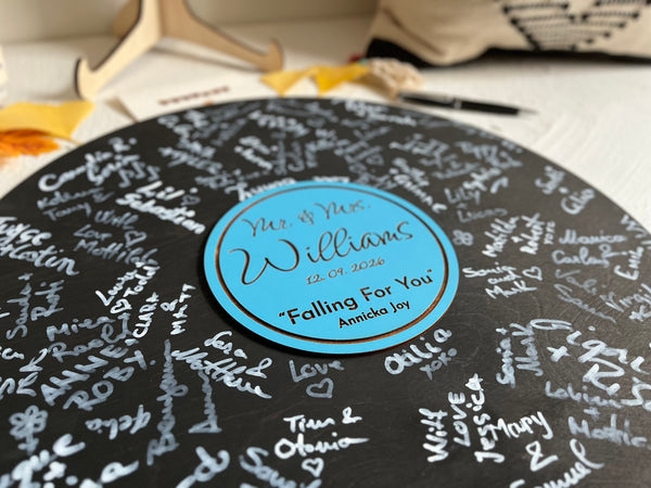 Vinyl music record lookalike sign used as a wedding guest book with personalized names, date and special song title and artist engraved in the middle. The wedding guests sign the record 