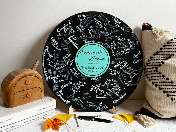 Vinyl music record lookalike sign used as a wedding guest book with personalized names, date and special song title and artist engraved in the middle. The wedding guests sign the record 