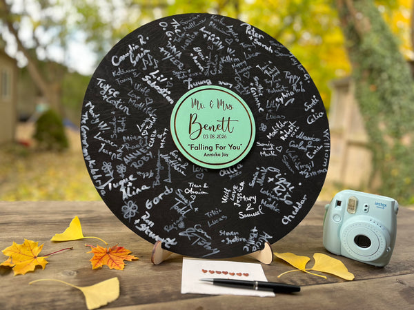 Vinyl music record lookalike sign used as a wedding guest book with personalized names, date and special song title and artist engraved in the middle. The wedding guests sign the record 