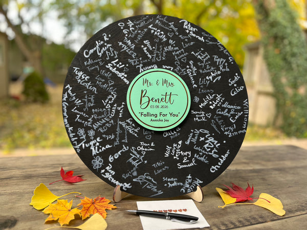 Vinyl music record lookalike sign used as a wedding guest book with personalized names, date and special song title and artist engraved in the middle. The wedding guests sign the record 