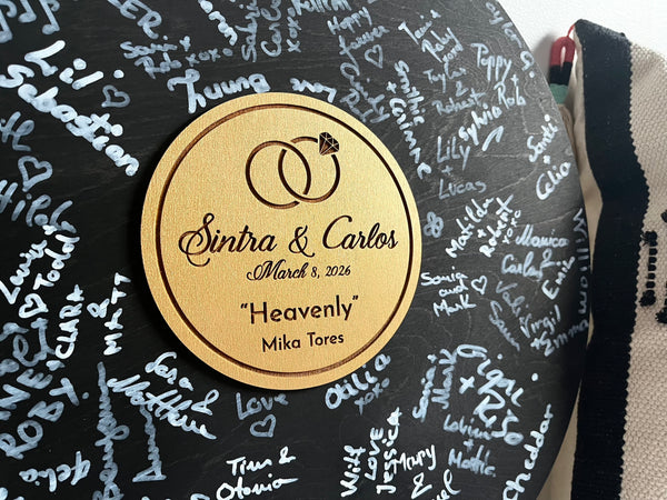 Black round vinyl record looking guest book made of wood for guest signatures, personalized with engraved text. The board is shown after the guests have signed it