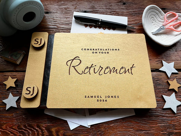 Personalized retirement guest book with golden covers engraved with text and the name of the retiree on a wooden surface with decorative items.