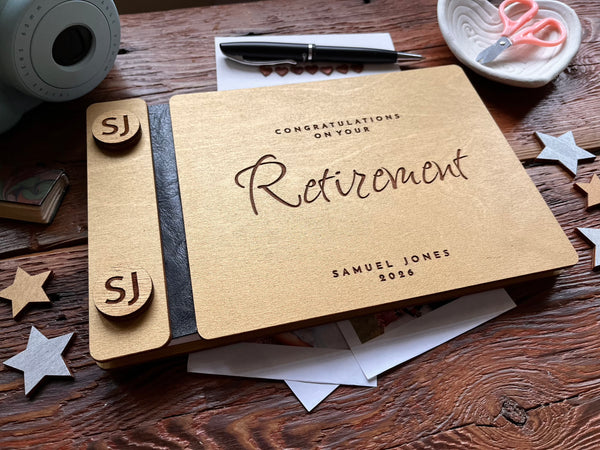 Personalized retirement guest book with golden covers engraved with text and the name of the retiree on a wooden surface with decorative items.