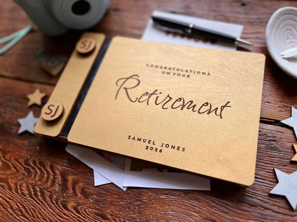 Personalized retirement guest book with golden covers engraved with text and the name of the retiree on a wooden surface with decorative items.