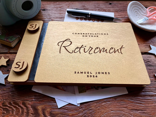 Personalized retirement guest book with golden covers engraved with text and the name of the retiree on a wooden surface with decorative items.