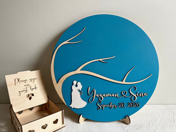 Personalized magnetic wedding sign with a couple silhouette and personalized text on a blue background, next to a wooden box with a guest book.