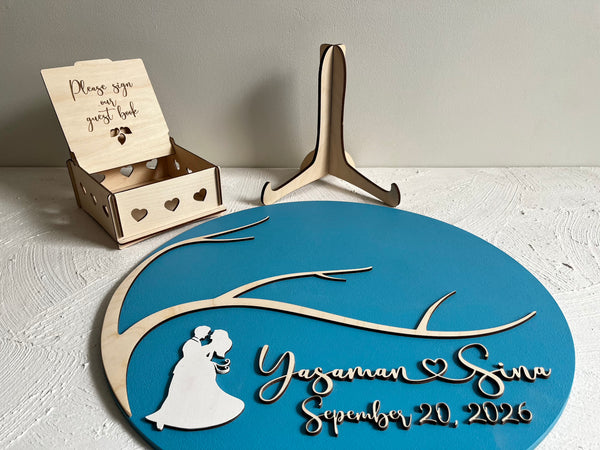 Decorative wedding sign with tree design, couple silhouette, and personalized text on a blue background.