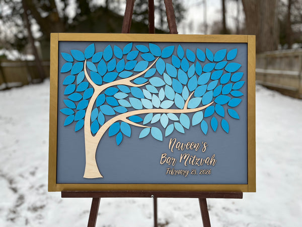 Decorative tree wall art for Bar Mitzvah with personalized detailswith blue leaves on a gray background, placed outdoors in winter.