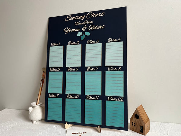 Seating chart for a wedding with tables and names on a dark navy board against a white wall. Made with personalized names for the bride and groom