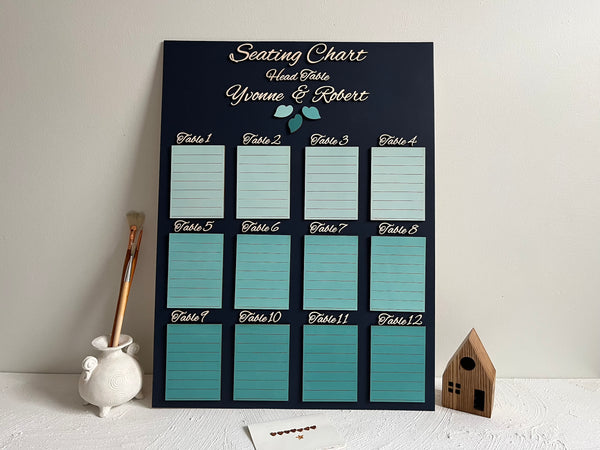 Seating chart for a wedding with tables and names on a dark navy board against a white wall. Made with personalized names for the bride and groom