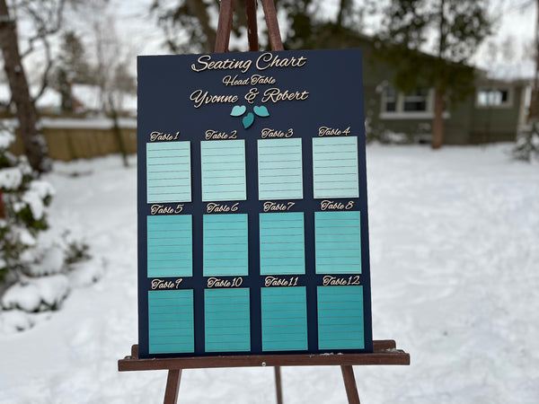 Seating chart for a wedding with tables and names on a dark navy board against a white wall. Made with personalized names for the bride and groom
