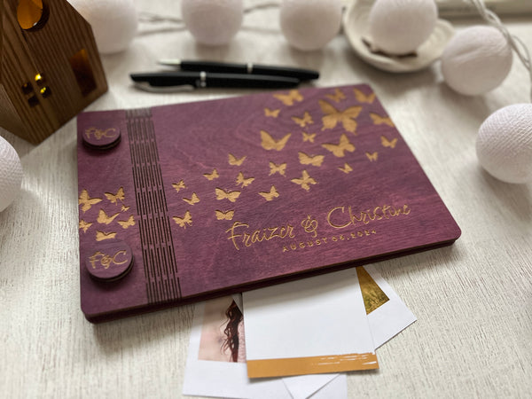 classic guest book for wedding custom engraved with the names of the bride and groom and butterflies on a purple stained wooden background