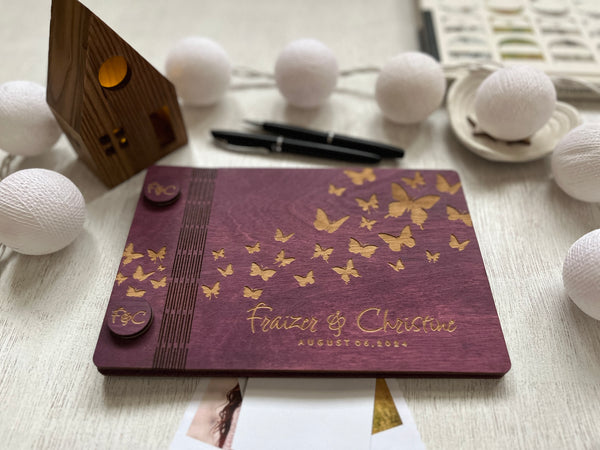 classic guest book for wedding custom engraved with the names of the bride and groom and butterflies on a purple stained wooden background