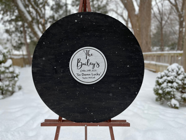 Black round sign with a label on an easel in a snowy outdoor setting