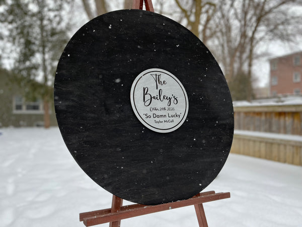 Black round sign with a white label on an easel in a snowy outdoor setting