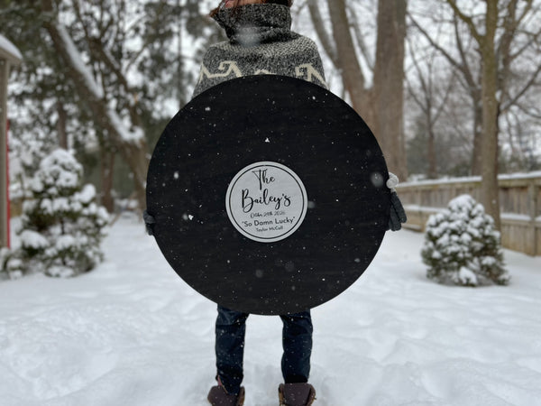 Person holding a large black circular sign with text in a snowy outdoor setting