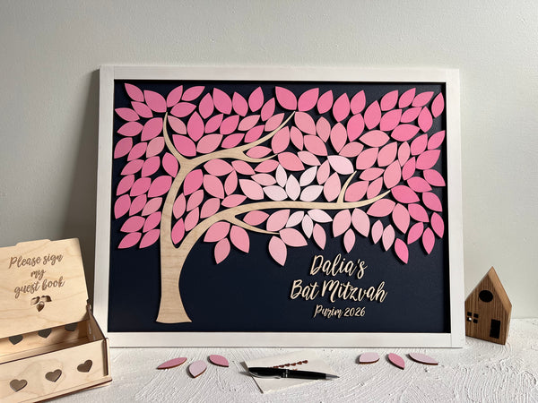 framed guest book alternative made for Bat Mitzvah featuring a tree with leaves to sign. The leaves are magnetic and removable from the magnetic background. The frame is white and the leaves are shades of cherry pink