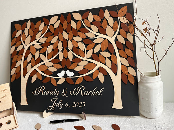 Personalized wedding guest book with magnetic removable leaves- each guest signs one leaf for the board. The board is rectangular, made with two trees that come into one, with the names of the bride and groom underneath and wedding date in script lettering. There is a box for storing leaves. 
