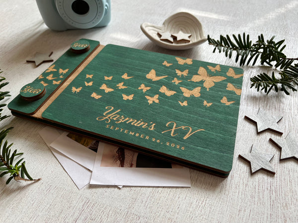 Green guest book album with gold butterfly patterns and 'Yazmin's XV' text on a light surface with decorative elements.