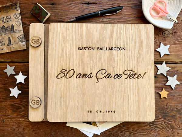 A personalized wooden keepsake album or notebook cover laid flat on a rustic wooden table, with the engraved text  '80 ans Ça ce Fête!', and a personalized name and year