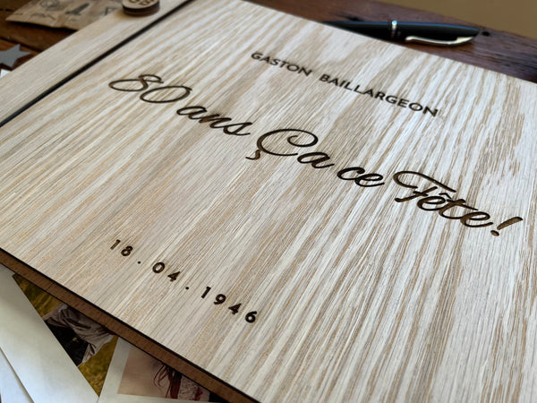 A close-up of a wooden keepsake album engraved with the text  '80 ans Ca ce Féte!', and a personalized name and date