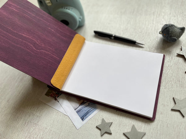 Open notebook with purple cover and yellow interior on a light surface with star-shaped objects and a camera.