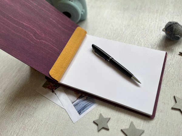 Open notebook with a pen on a light wooden surface with star-shaped objects.