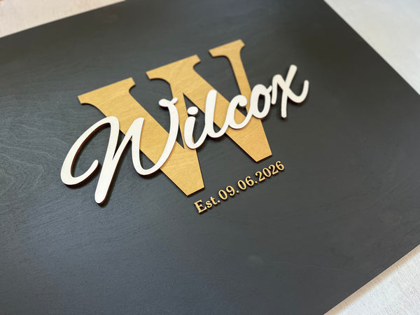 Last name sign with monogram and established date, on a wooden background with customizable colors - example on a black background, gold monogram, white text, gold date