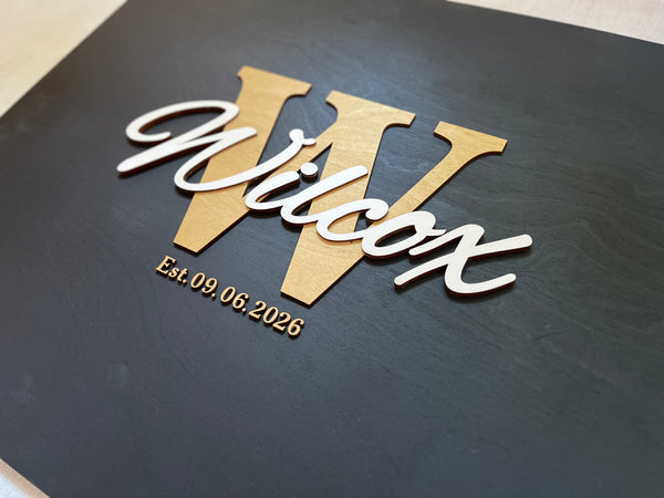 Last name sign with monogram and established date, on a wooden background with customizable colors - example on a black background, gold monogram, white text, gold date