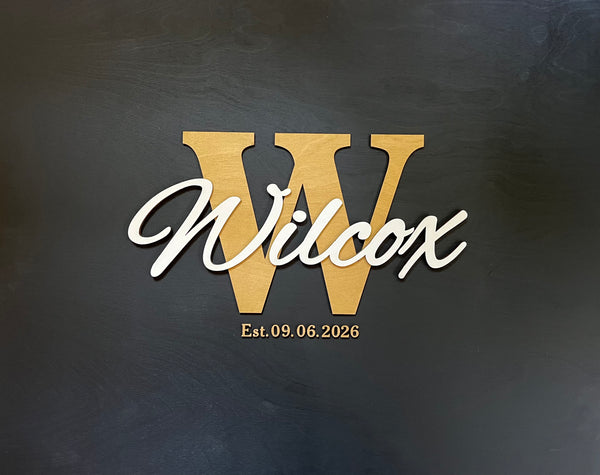 Last name sign with monogram and established date, on a wooden background with customizable colors - example on a black background, gold monogram, white text, gold date