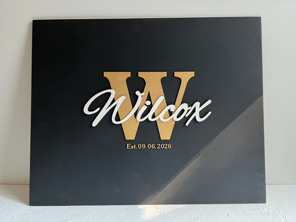 Last name sign with monogram and established date, on a wooden background with customizable colors - example on a black background, gold monogram, white text, gold date