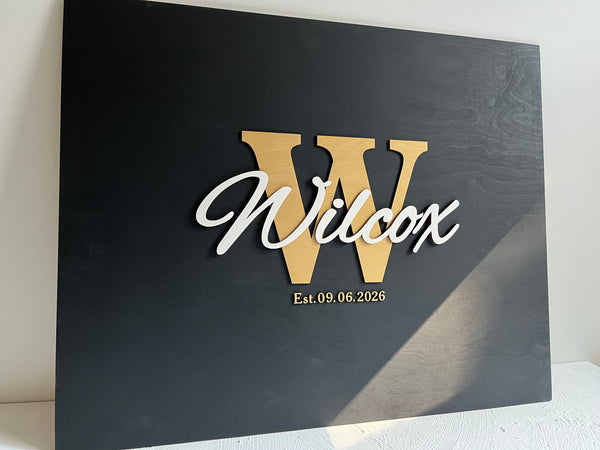 Last name sign with monogram and established date, on a wooden background with customizable colors - example on a black background, gold monogram, white text, gold date