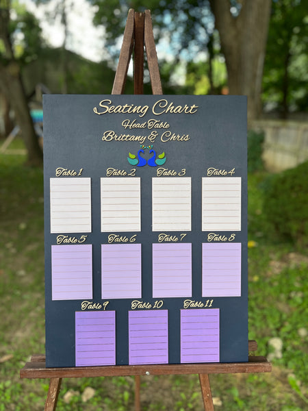 Seating chart for a wedding on a wooden stand outdoors with trees in the background.