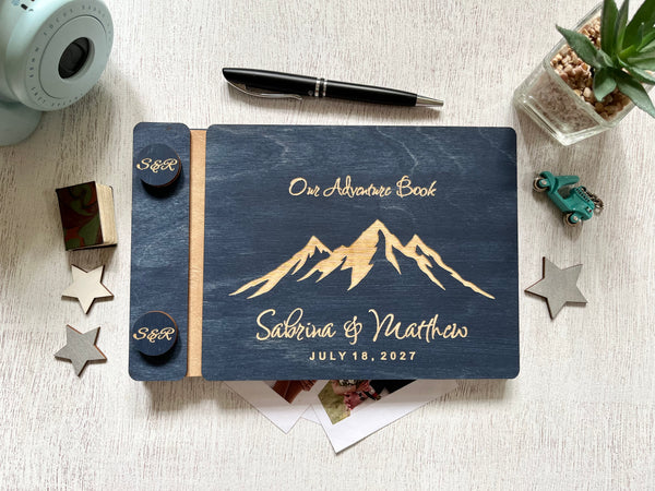A personalized wooden keepsake journal titled 'One Adventure Book' with mountain artwork and personalized names  on the cover, styled in white decor.