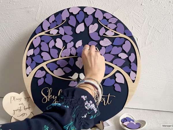 A hand signing a magnetic leaf in purple and placing the leaf on the magnetic wedding guest book alternative with magnetic leaves