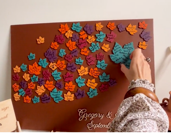 Decorative magnetic guest book with colorful leaf patterns and personalized text on a brown background with maple leaves. Each leaf is magnetic and can be signed and added to the background.