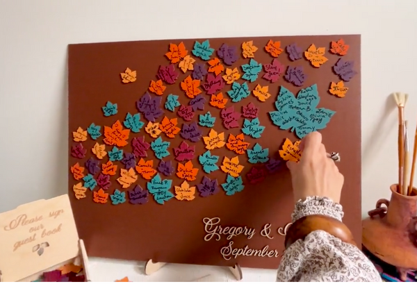 Decorative magnetic guest book with colorful leaf patterns and personalized text on a brown background with maple leaves. Each leaf is magnetic and can be signed and added to the background.