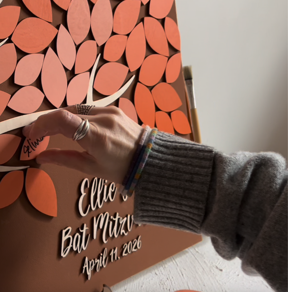 Hand placing a leaf-shaped cutout on a decorative wall with personalized Bat Mitzvah text.