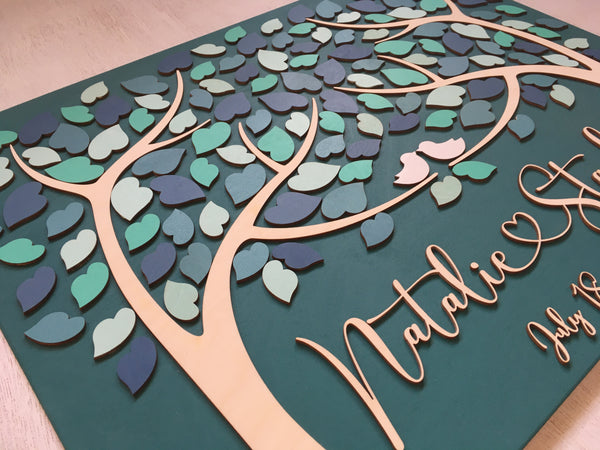calligraphic font with a heart in between the names on a teal guestbook alternative with two trees