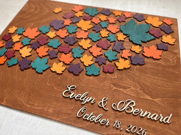 Wooden board with colorful maple leaf-shaped cutouts and personalized  names and date- used as a wedding guest book alternative for guest signatures